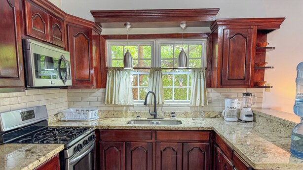 A kitchen with dark wood cabinets, a granite countertop, stainless steel appliances, and a window with curtains. - Studio Apartment In Hopkins (Hopkins)