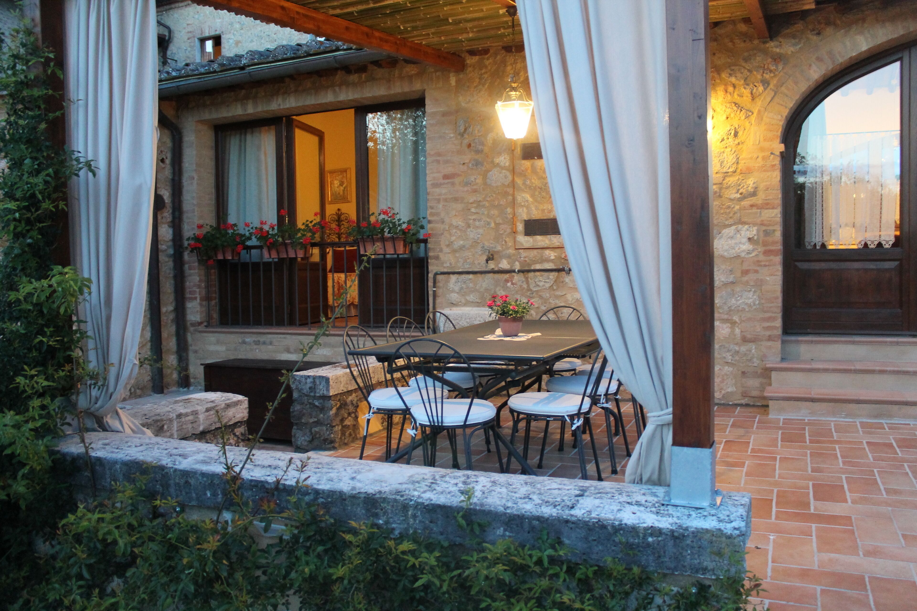 Eine Terrasse im Freien mit einem Steintisch und -stühlen, umgeben von Steinmauern und einer Holzpergola.
