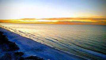 A coastal landscape with a beach and ocean during sunset.