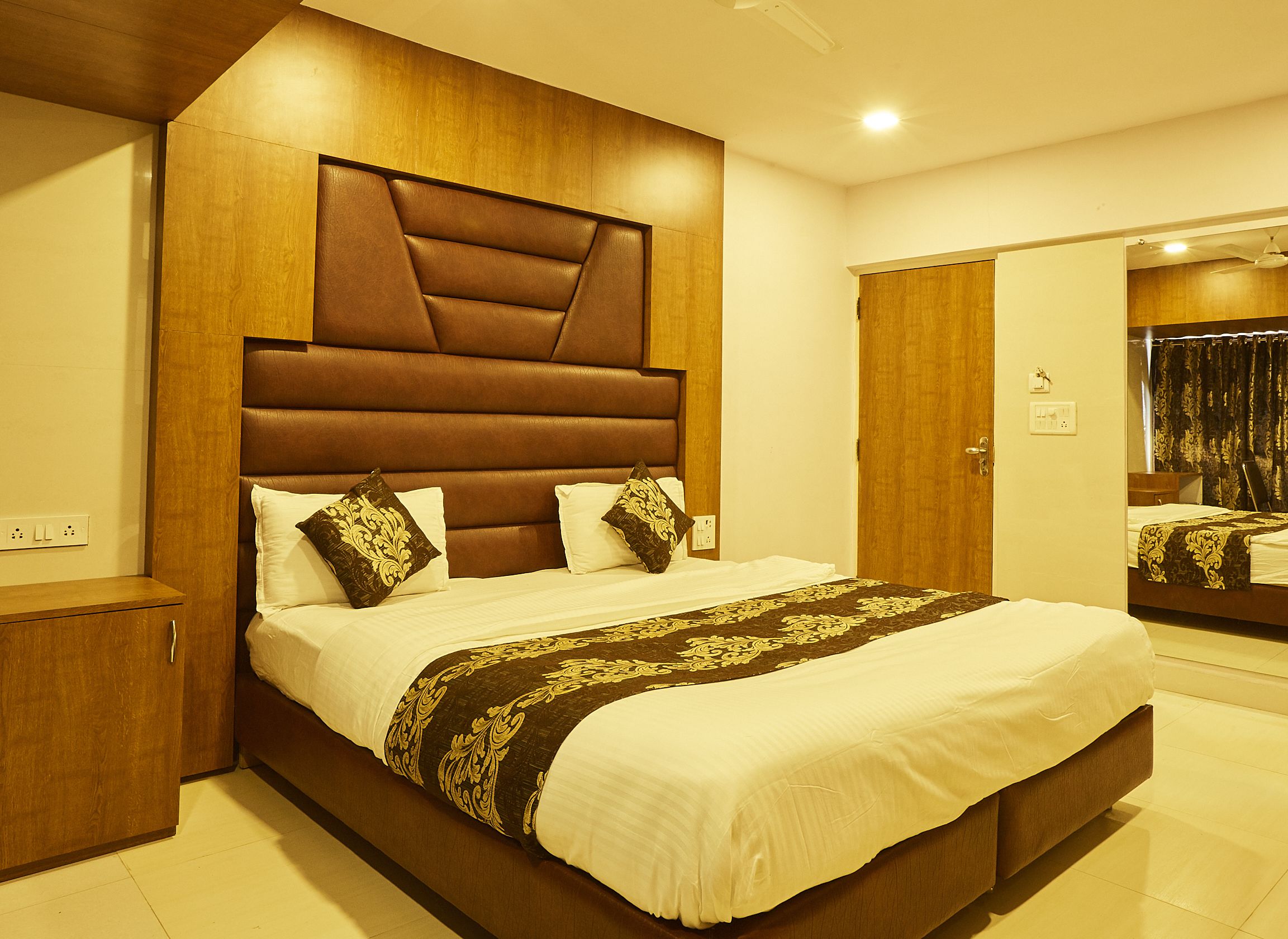 A modern hotel room with a large bed, wooden headboard, and a mirror on the wall.