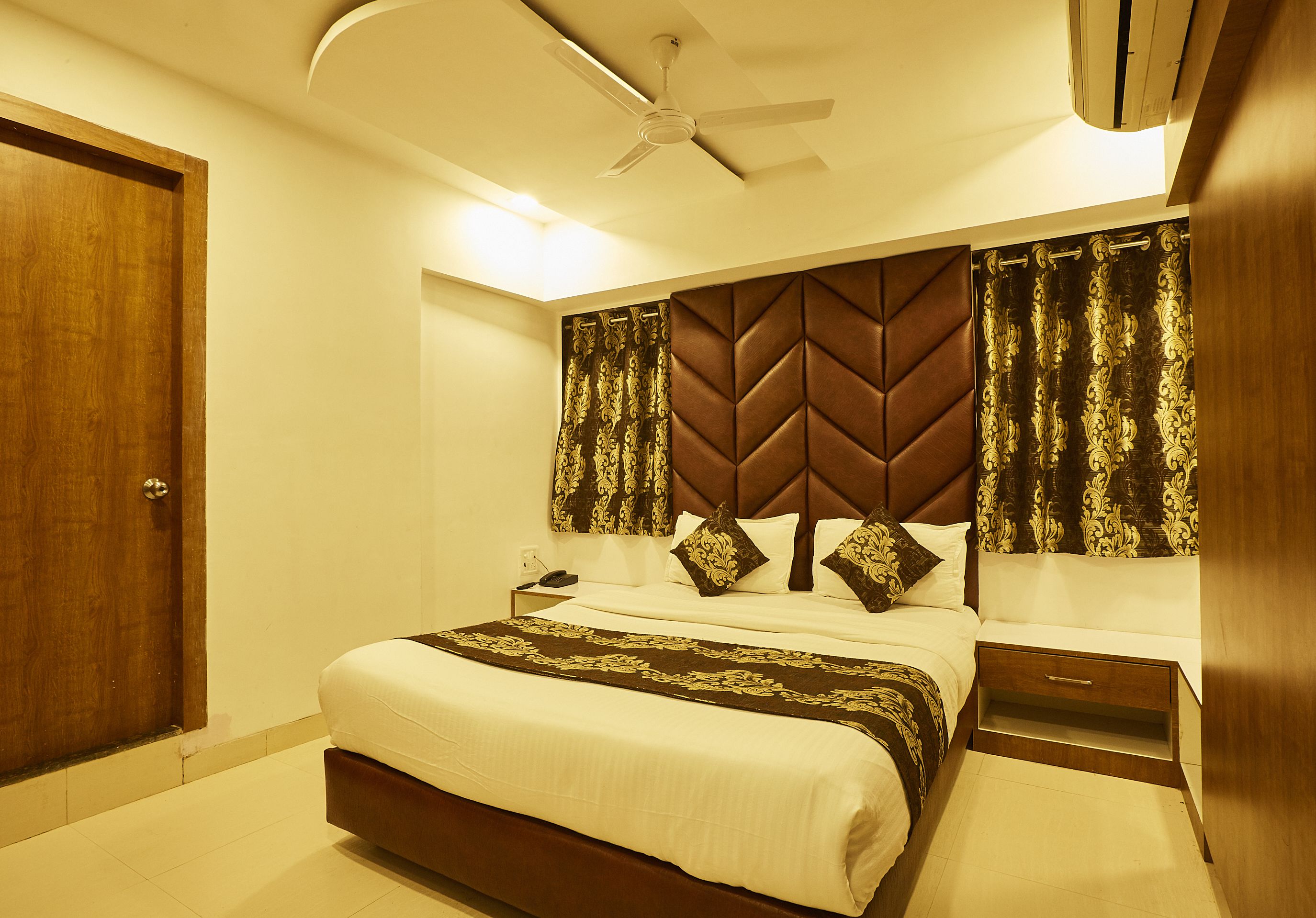 A hotel room with a bed, bedside table, nightstand, and a ceiling fan.