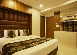 Una habitación de hotel con una cama grande, cabecera de madera, mesita de noche, unidad de aire acondicionado y una puerta.