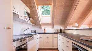 A modern kitchen with wooden beams, a skylight, and a view of greenery outside.