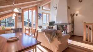 A cozy living room with a wooden ceiling, a fireplace, and a dining area with a table and chairs.