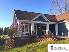 A two-story house with a stone foundation, a front porch with white columns, and a number '6413' on the house. - Porch Swing Saugatuck - Modern Farmhouse + Hot Tub, EV Charger, Billiards, Bikes (Saugatuck)
