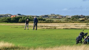 En golfbana med klar himmel, hus i bakgrunden och en barnvagn i förgrunden.
