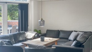 Ett modernt vardagsrum med en soffa, fåtöljer, ett soffbord och en hängande lampa.