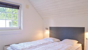 Ett sovrum med en enkel säng, ett fönster med persienner, en vägglampa och ett element.