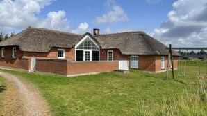 Ett traditionellt hus byggt av tegel med ett halmtak, ett fönster mitt på fasaden och en liten veranda.