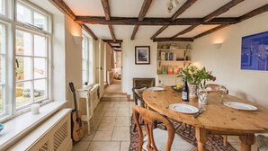 A dining area with a wooden table set for two, a guitar leaning against the wall, and a view through the window. - Little Chart, Deal, Kent (Deal)