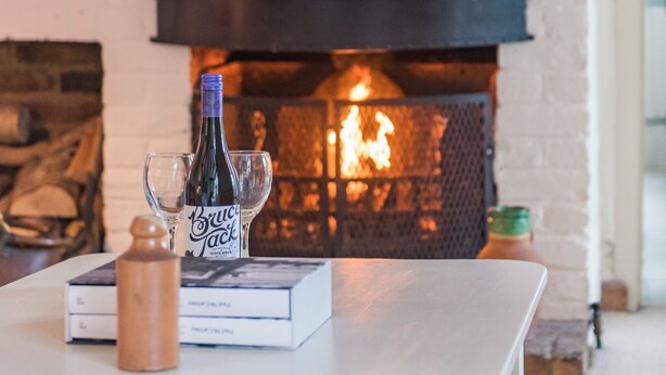 A fireplace with a lit fire, a white table with a bottle and glass, and a mirror above the mantel. - Little Chart, Deal, Kent (Deal)