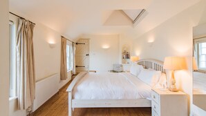 A bedroom with a large bed, a nightstand with a lamp, a chest of drawers, a radiator, and a window with curtains. - Little Chart, Deal, Kent (Deal)