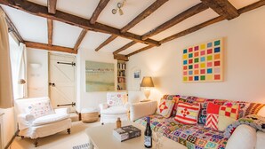 A cozy living room with a white sofa, a white armchair, and a coffee table with a bottle and glasses. There is a bookshelf and a colorful quilt on the sofa. - Little Chart, Deal, Kent (Deal)