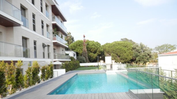 A modern outdoor swimming pool with a wooden deck, surrounded by greenery and a multi-story building with balconies. - Ripple - near Congress Centre & River- A/C, swimming, pool, secure parking (Lisboa)