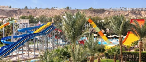Parque acuático con toboganes y una piscina rodeada de palmeras.