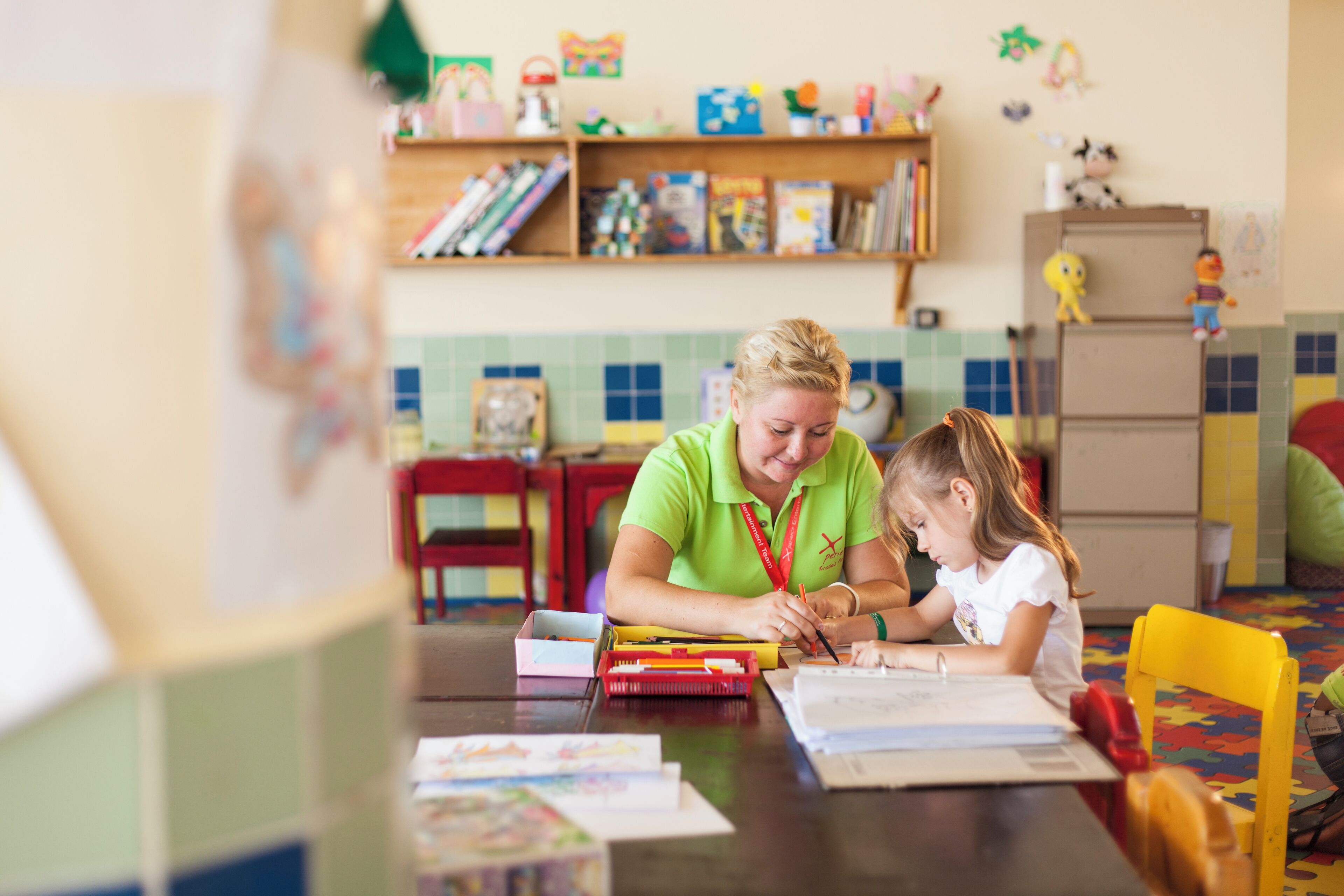 Un aula con un profesor y un niño sentados en una mesa, rodeados de material educativo y juguetes.
