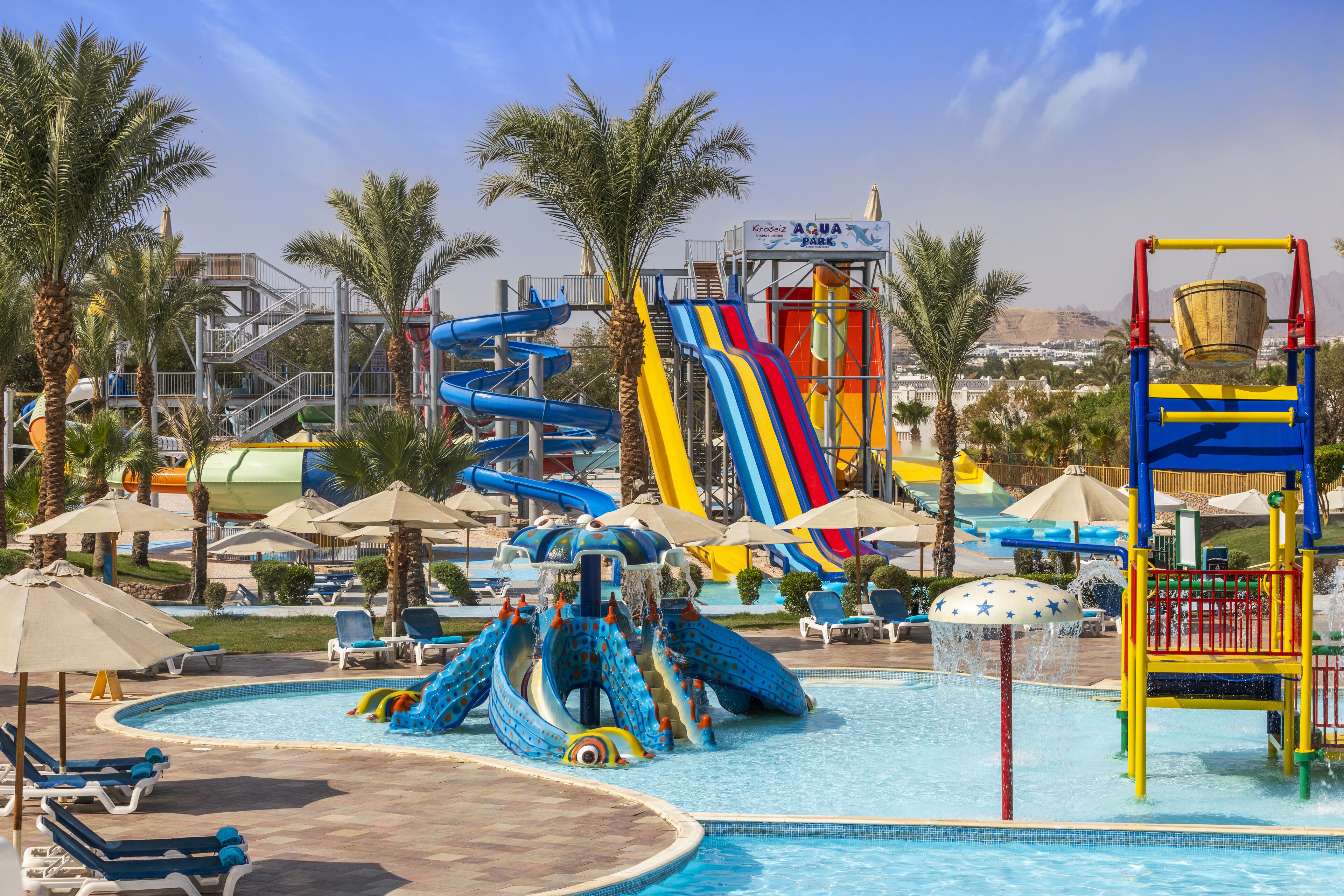 Un parc aquatique avec des toboggans, une piscine et des palmiers.