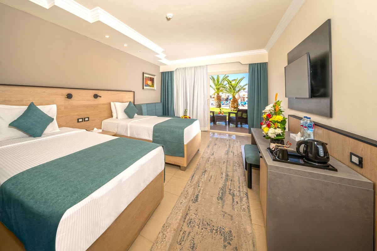 A hotel room with two beds, a desk, a TV, and a view of the pool area.