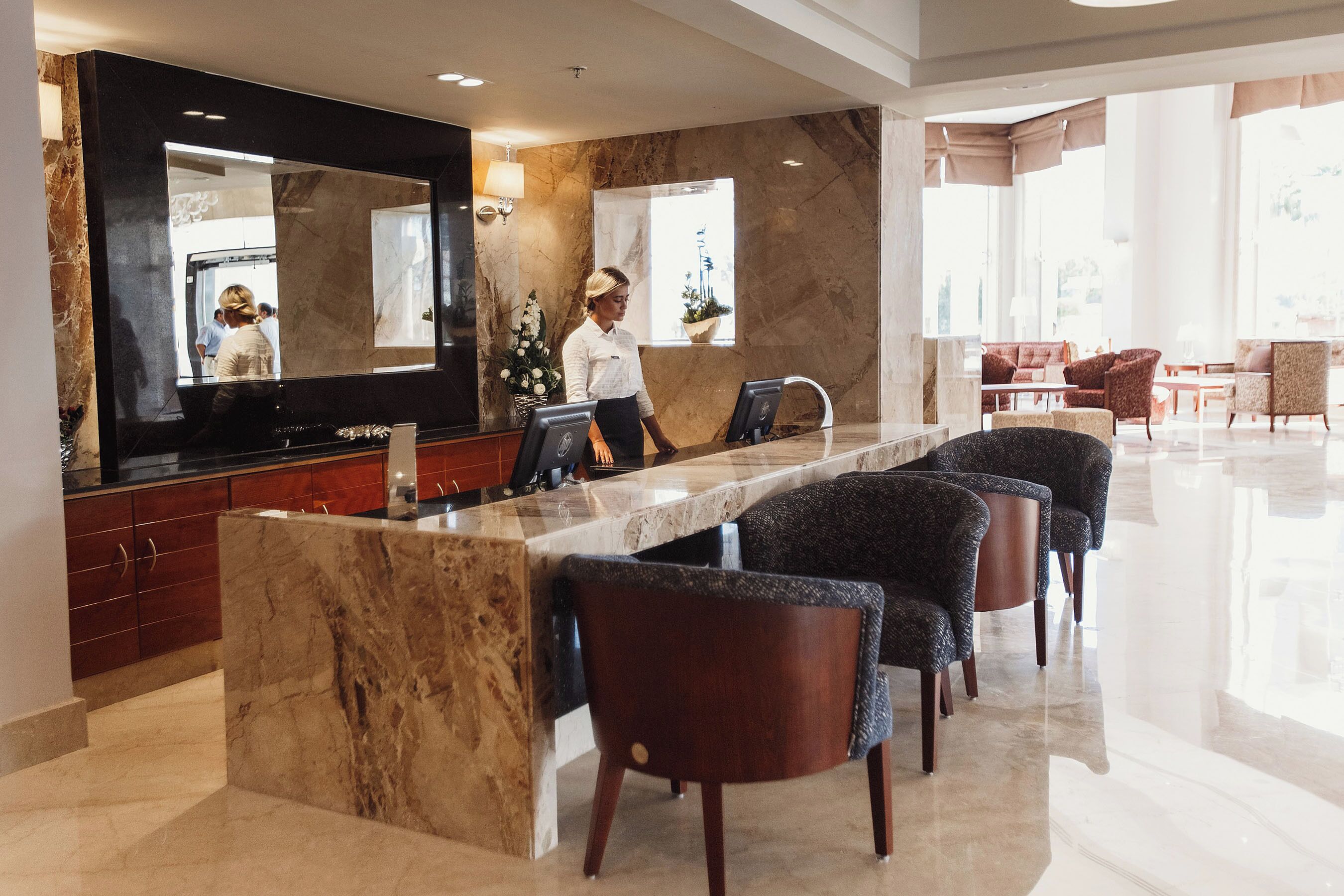 Un hall d’hôtel doté d’un comptoir d’accueil en marbre, d’un espace salon et de grandes fenêtres.