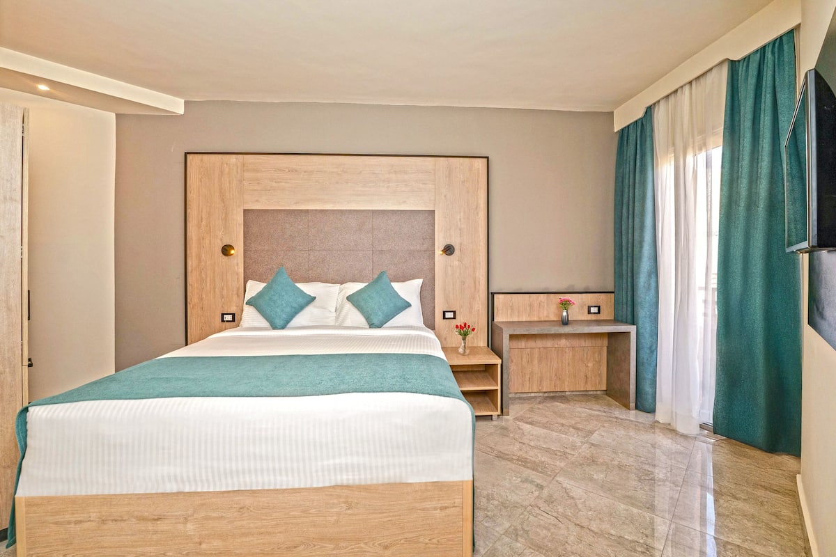 A hotel room with a wooden bed, a nightstand, a vase with flowers, and a TV on the wall.
