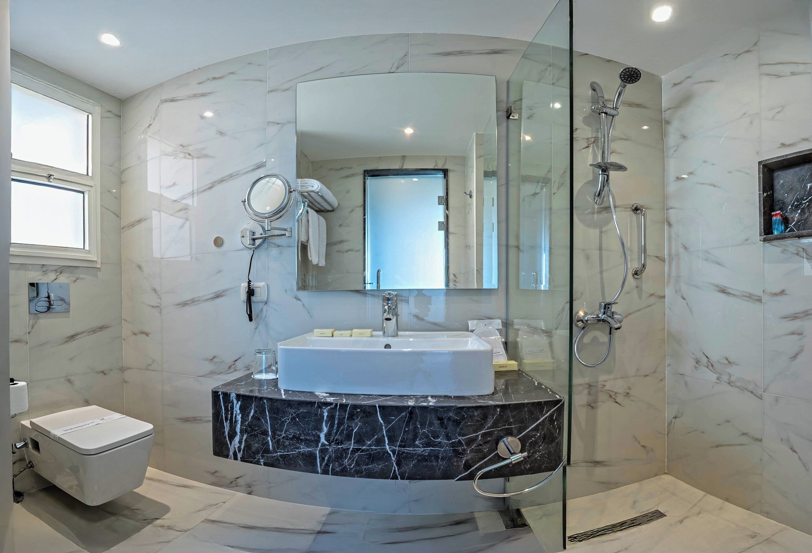 Une salle de bain moderne avec une douche à parois de verre, un lavabo blanc et un meuble-lavabo recouvert de carreaux de marbre.