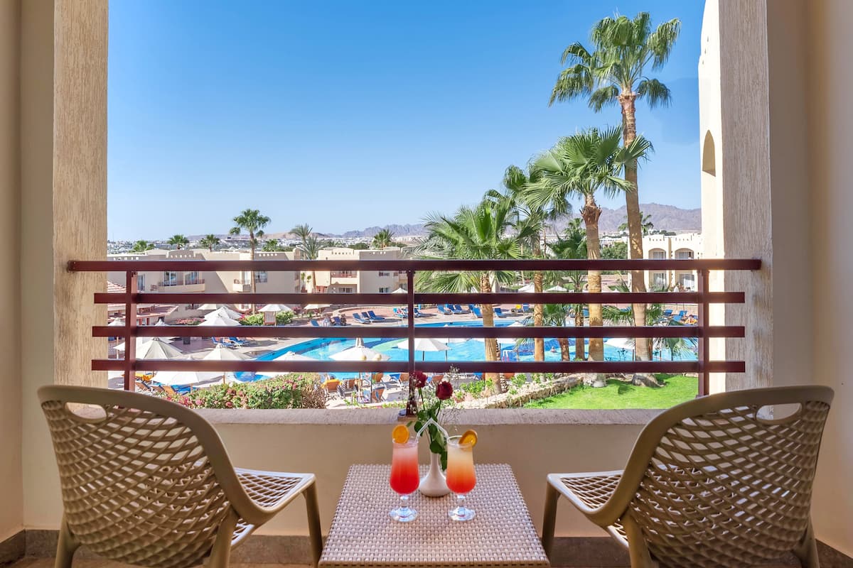 A balcony with wicker chairs and a table, overlooking a pool and palm trees.