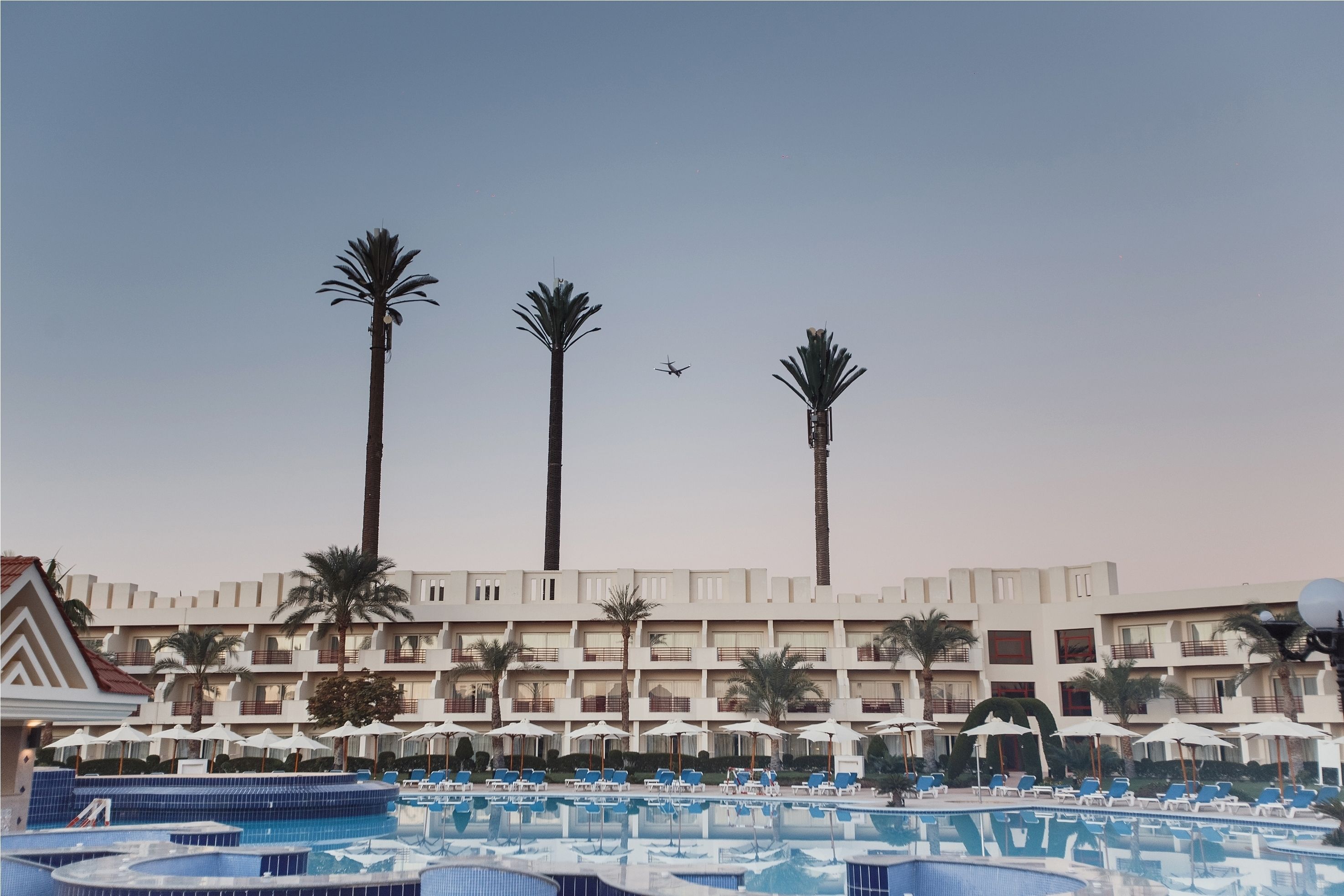 A hotel with multiple floors, a swimming pool, and palm trees.