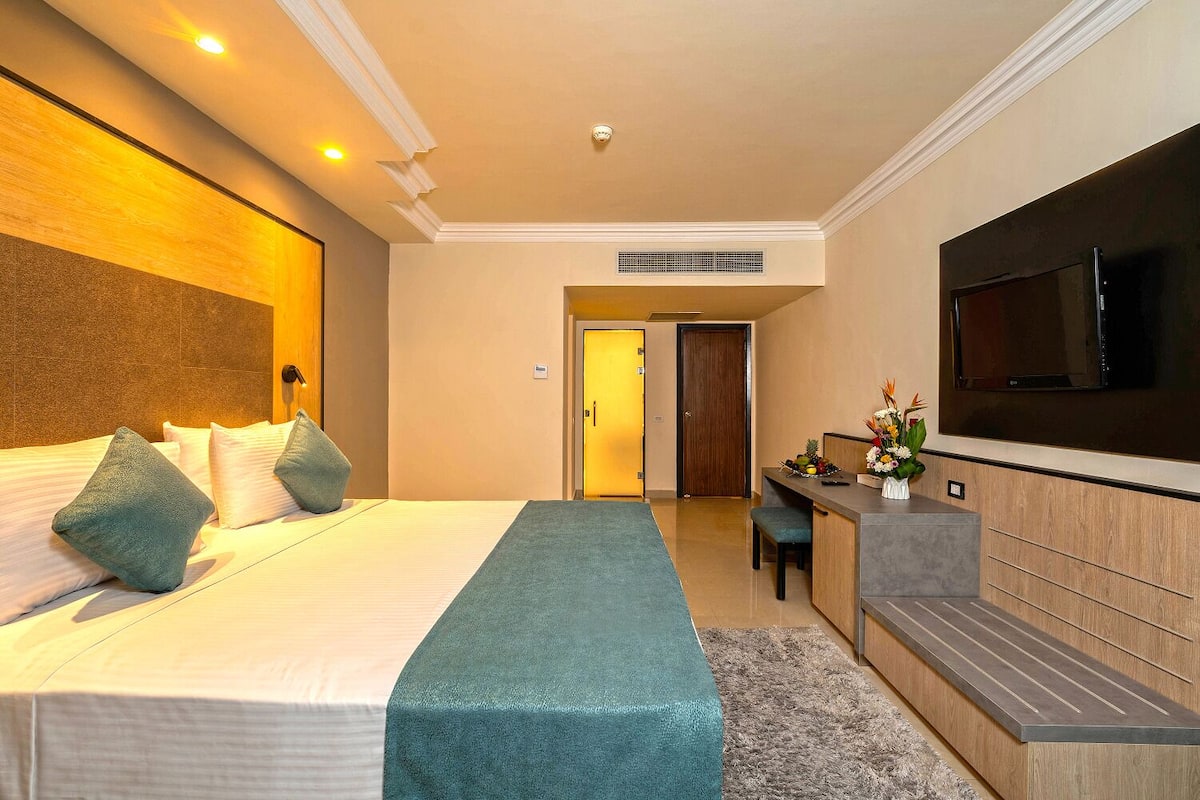 A hotel room with a large bed, a desk, a flat-screen TV, and a bathroom door.