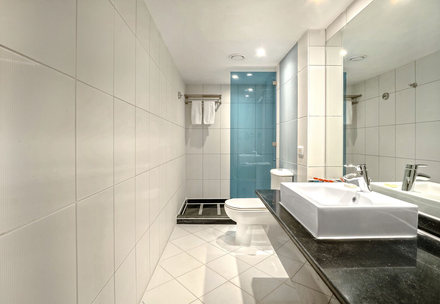 A modern bathroom with white and blue tiles, a black countertop, a white sink, and a large mirror.