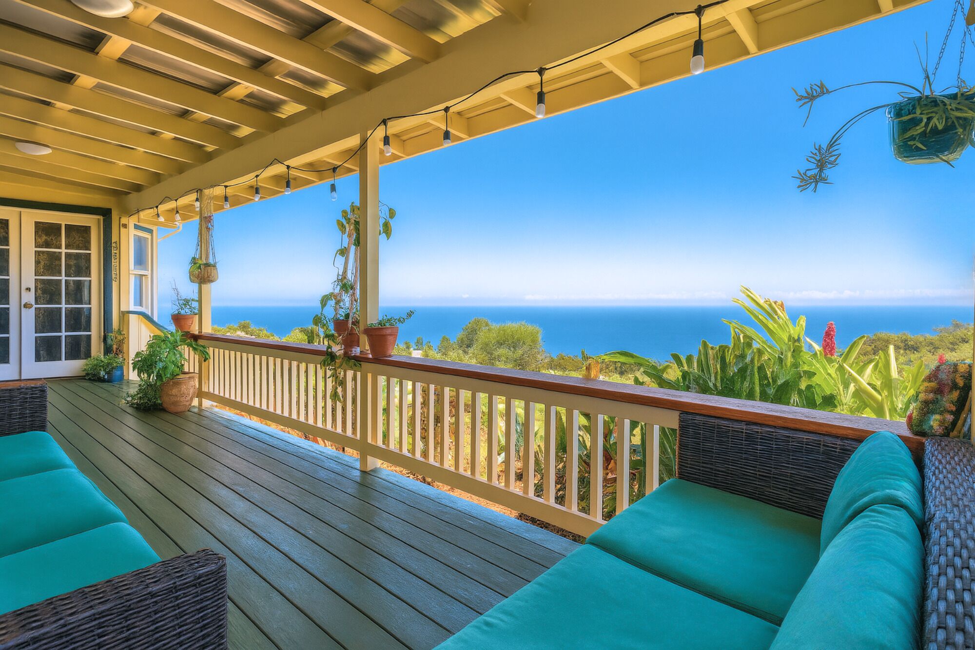 A covered outdoor deck with wooden flooring, green cushioned seating, and hanging planters.