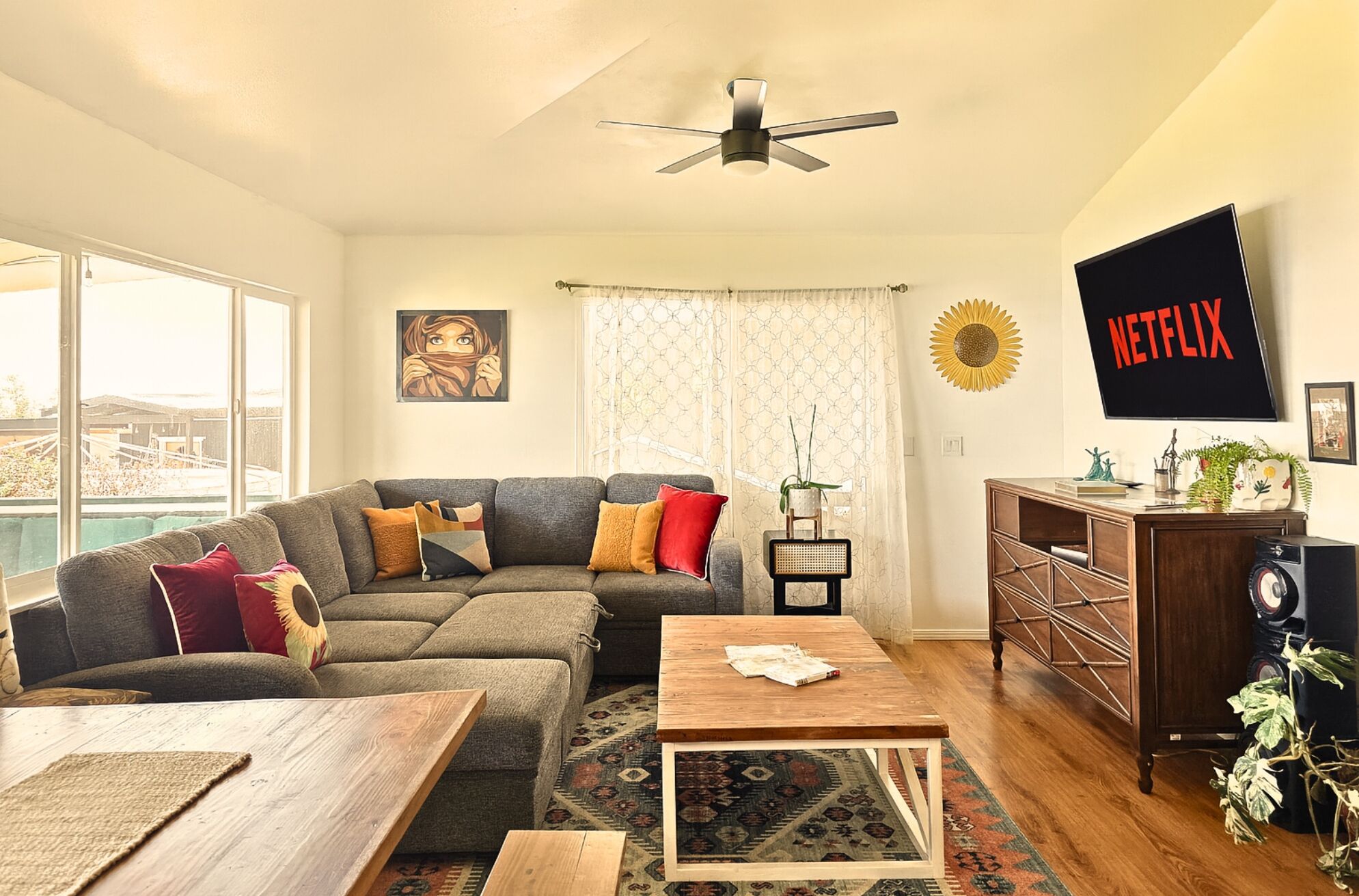 A living room with a sectional sofa, a coffee table, a TV mounted on the wall, and a ceiling fan.