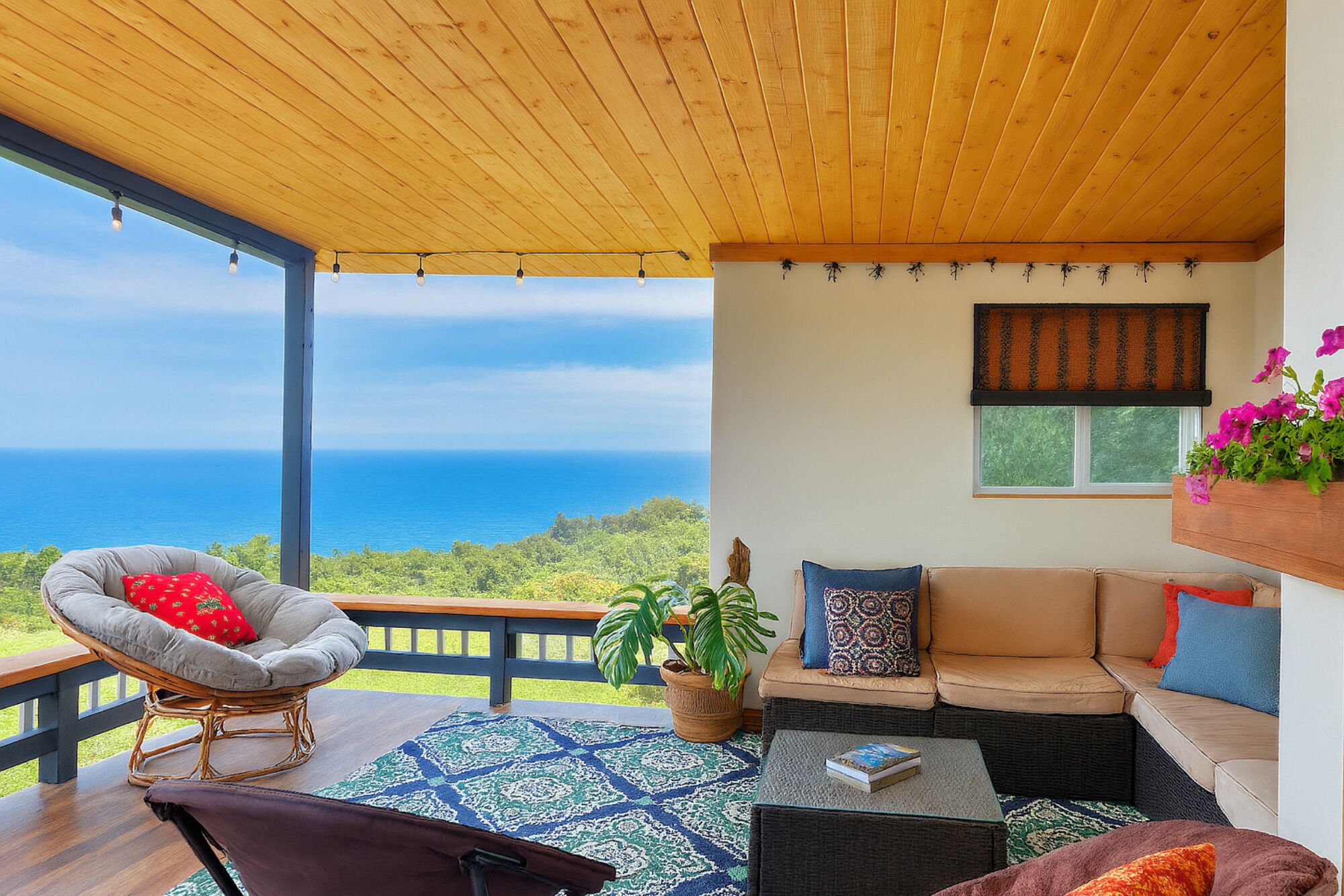 A balcony with a view of the ocean, wicker furniture, a sofa, and a potted plant.