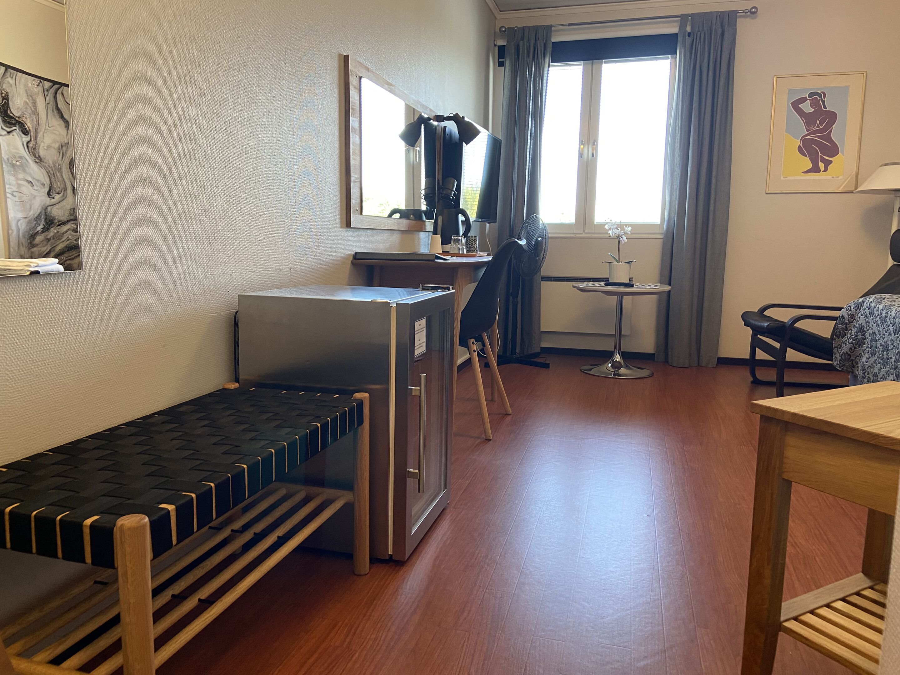 Quarto de hotel pequeno, com uma cama de solteiro, cozinha compacta, área de refeições e janela com cortinas.