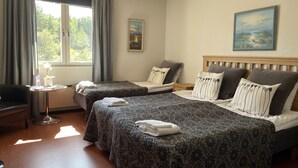 Une chambre d’hôtel avec deux lits, une petite table sur laquelle se trouvent une bouteille et des verres, une chaise et une fenêtre avec des rideaux.