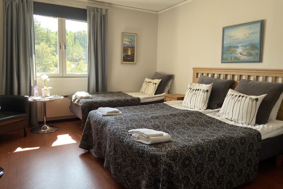 Une chambre d’hôtel avec deux lits, une petite table sur laquelle se trouvent une bouteille et des verres, une chaise et une fenêtre avec des rideaux.