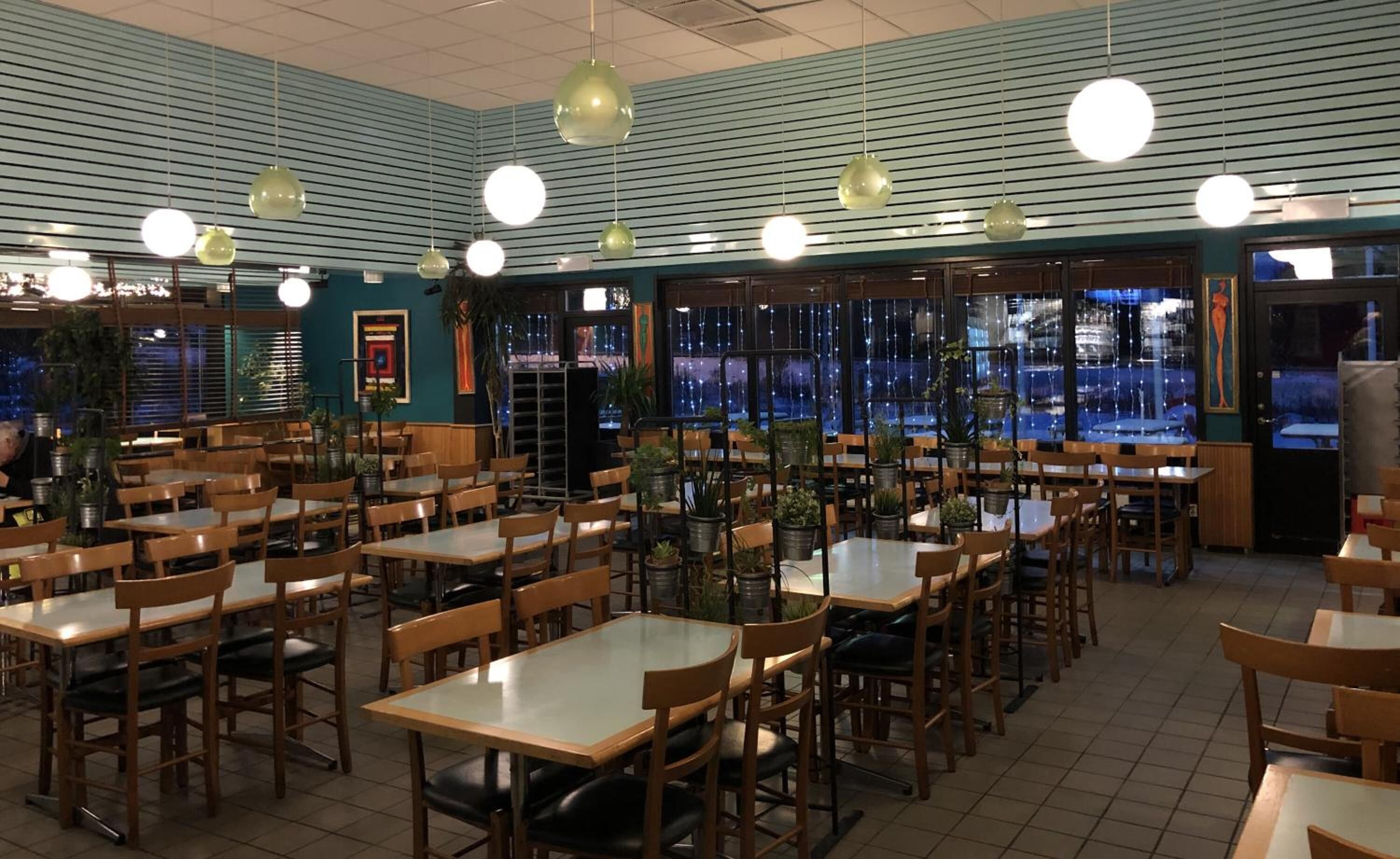 Un restaurant spacieux, doté de nombreuses tables et chaises, de grandes fenêtres offrant une vue agréable et de luminaires suspendus.