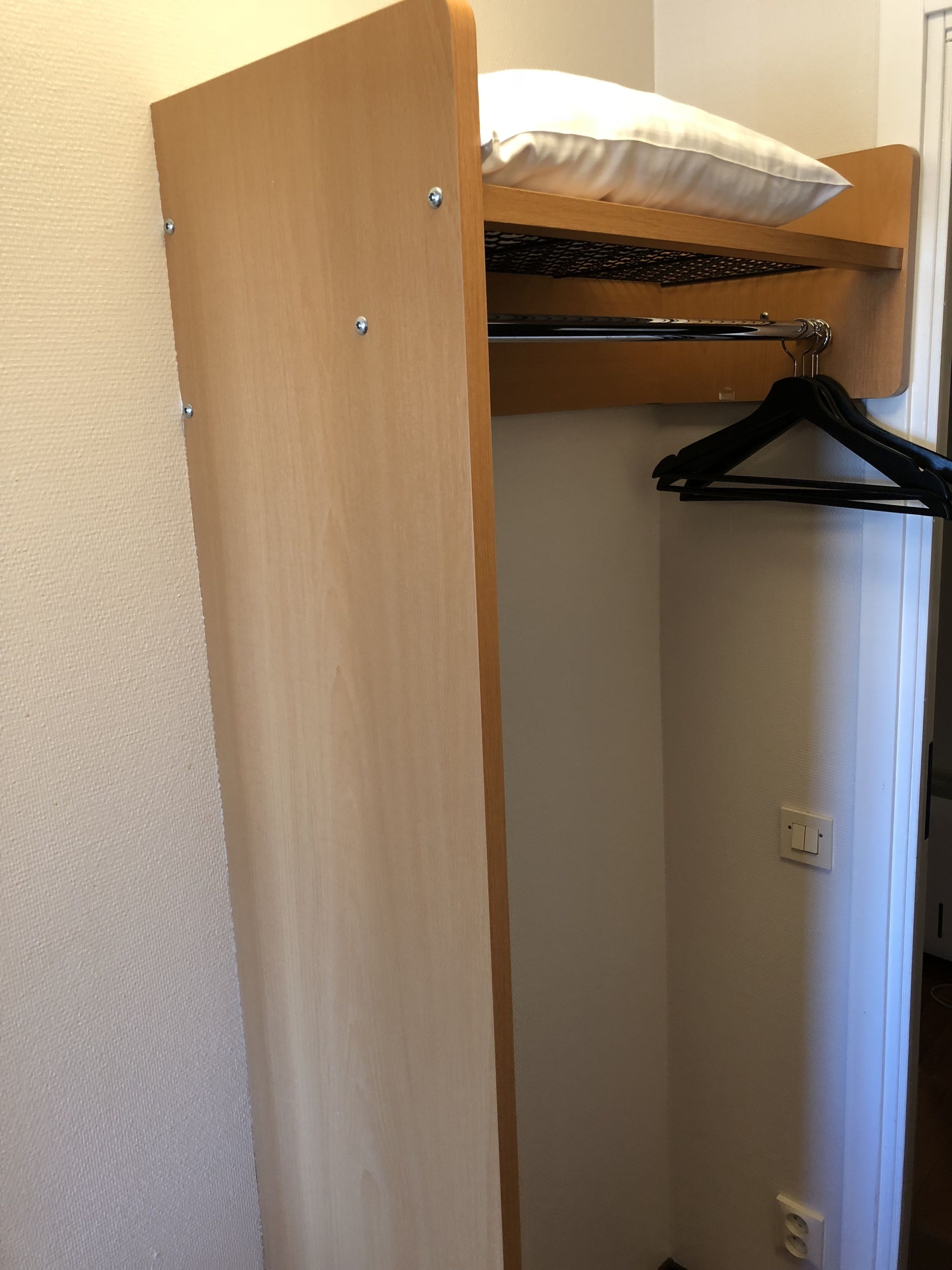 Un armario de madera con espacio para colgar y un interruptor de luz en la pared.