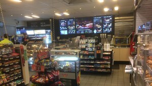 L’intérieur d’une épicerie de proximité, avec un présentoir réfrigéré, des étagères remplies de collations et un panneau affichant le menu.