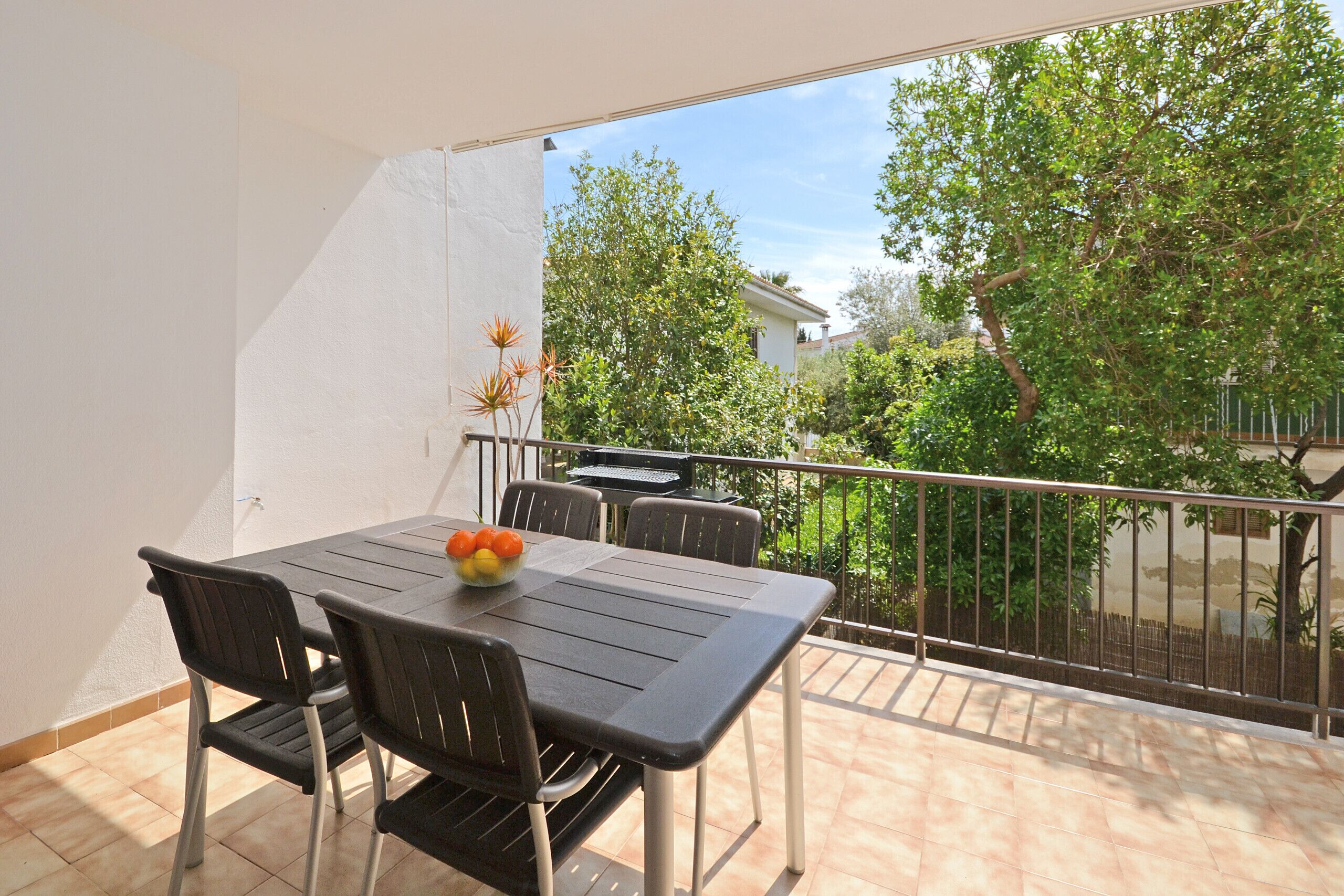 Un balcon avec une table et des chaises, un barbecue et une vue sur la verdure et les bâtiments.