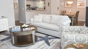 A living room with a striped sofa, a round coffee table, and a dining area with a table and chairs. - Beachy Getaway–Cozy, Clean & Equipped w/ All Essentials! Relax, Enjoy & Refresh! (St Augustine Beach)