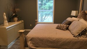 A bedroom with a large bed, a dresser, a window with blinds, and a lamp.