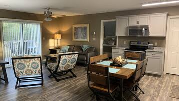 A modern kitchen with white cabinets, a microwave, and a stove. There is a dining area with a wooden table and chairs.