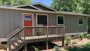 A single-story mobile home with a front porch, a red door, and a small deck.