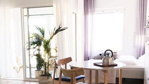 A bright, modern living room with a wooden dining table, two chairs, a sofa, and a large potted plant. - Roost Lauttasaari (Helsinki)