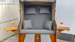 Un sofá cama convertible con cojines a rayas y un dosel, dos mesitas de noche con vasos de jugo de naranja, y un piso de madera.