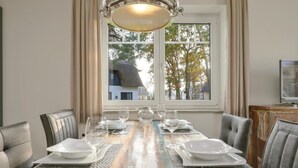 Mesa de comedor preparada para seis personas, con vistas a árboles y una casa a través de un amplio ventanal.