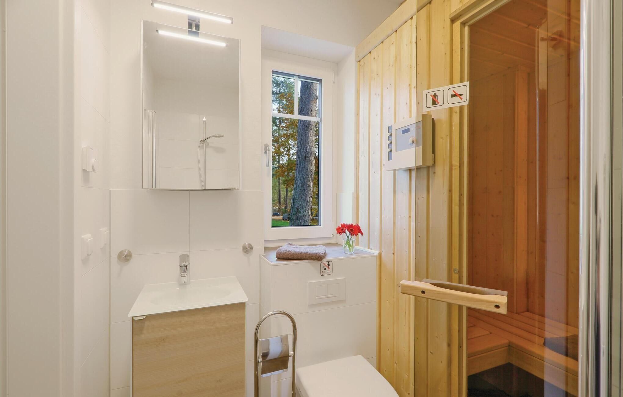 Une salle de bain moderne avec une douche à l’italienne en verre, un lavabo et une fenêtre donnant sur la verdure.
