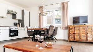 Una cocina moderna con armarios blancos, horno empotrado y comedor con mesa y sillas de madera.