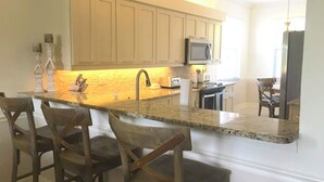 A kitchen with a granite countertop, wooden chairs, a microwave, and a sink.