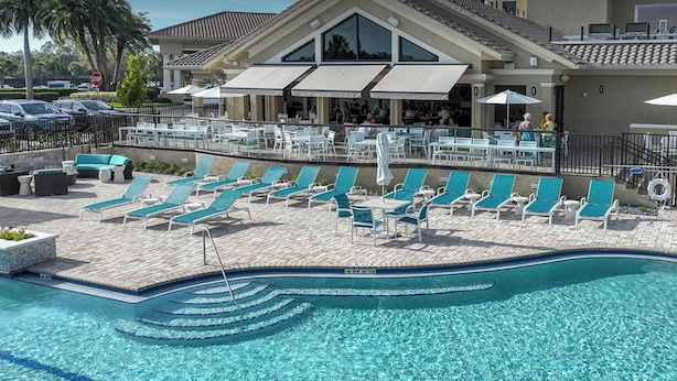 A pool area with lounge chairs and umbrellas, a covered seating area, and a building with a tiled roof in the background.